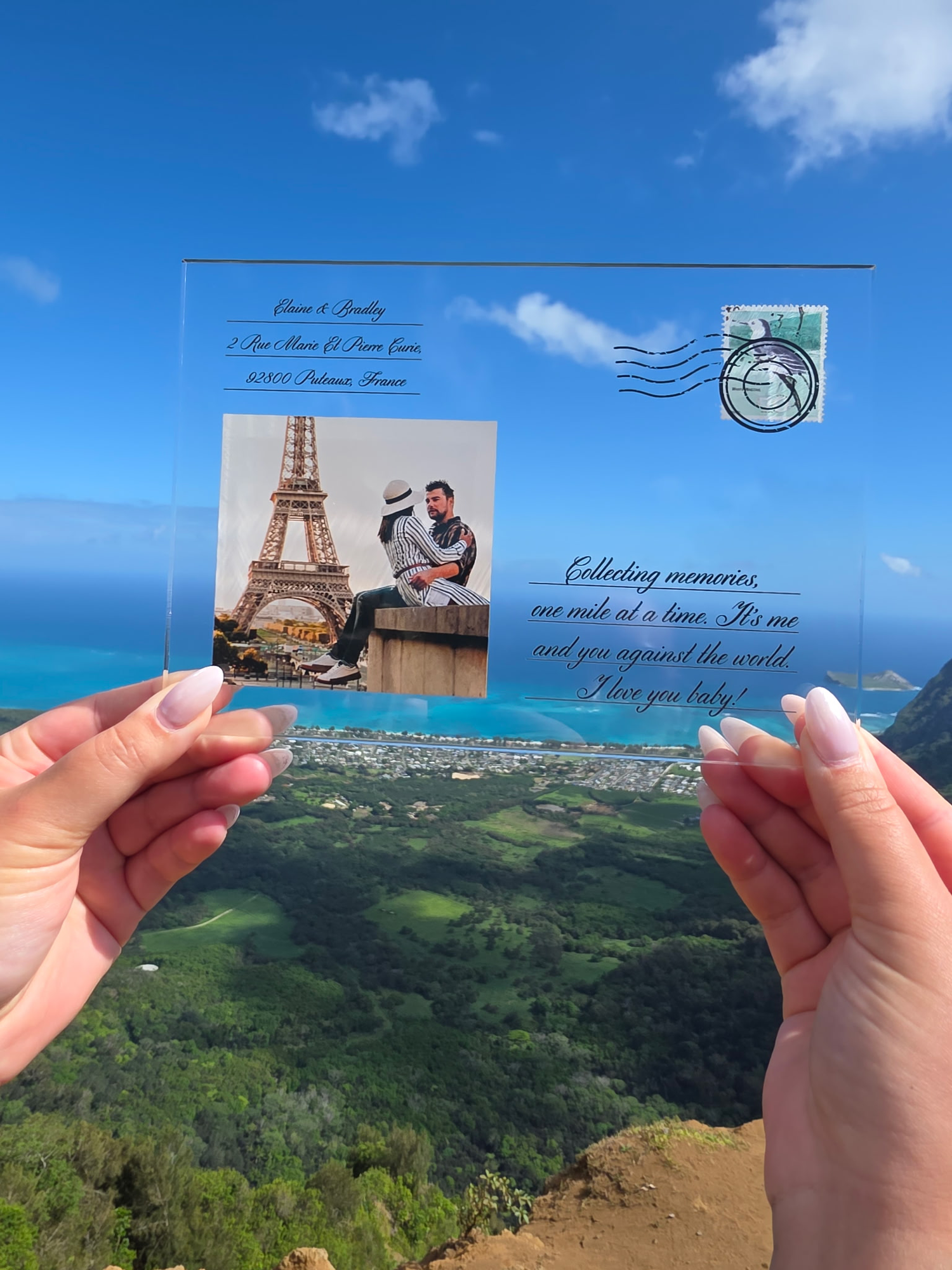 Person holding a custom transparent acrylic printed postcard with a couple at the Eiffel Tower against a scenic background.